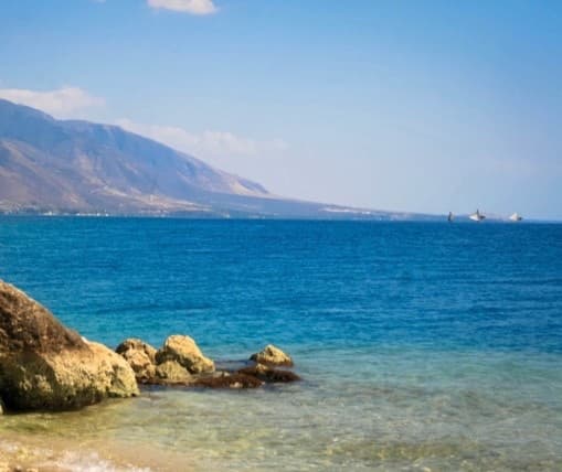 The Haitian coast: clear water over rocks in the foreground and mountains across the bay behind