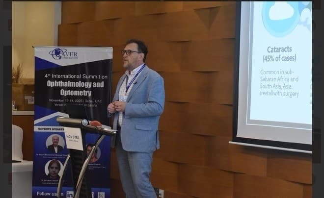 Kerry Reeves speaking beside the banner for the 4th International Summit on Ophthalmology and Optometry in Dubai